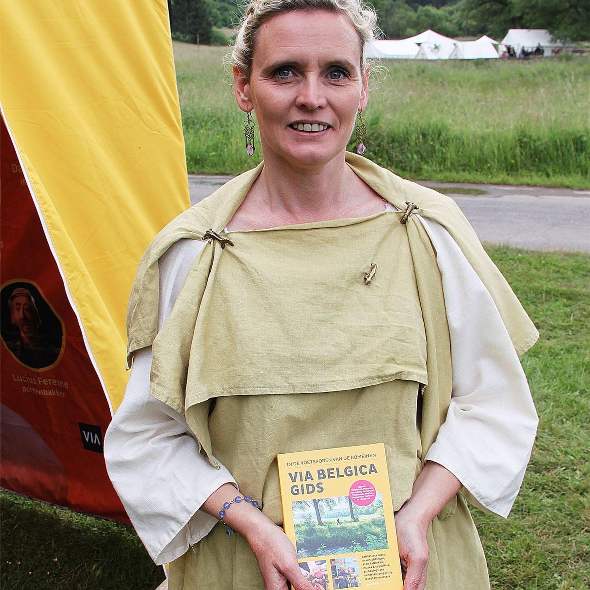 Anja Neskens trägt eine römische Tunika und hält ein Buch mit dem Titel: „Via Belgica Gids“ in den Händen.