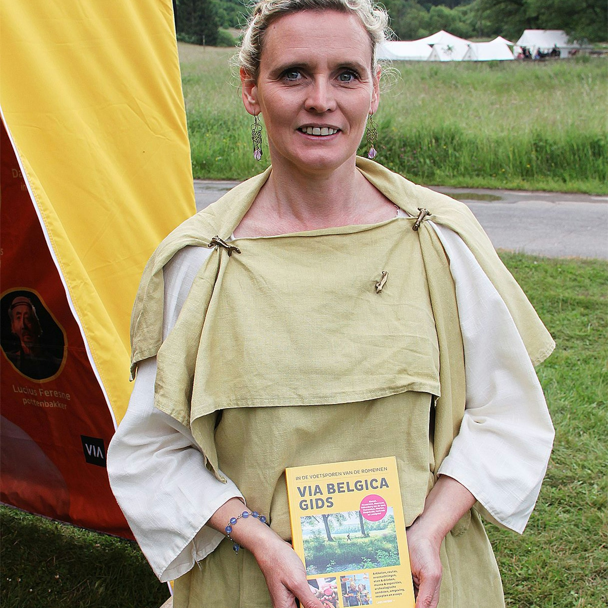 Anja Neskens trägt eine römische Tunika und hält ein Buch mit dem Titel: „Via Belgica Gids“ in den Händen.