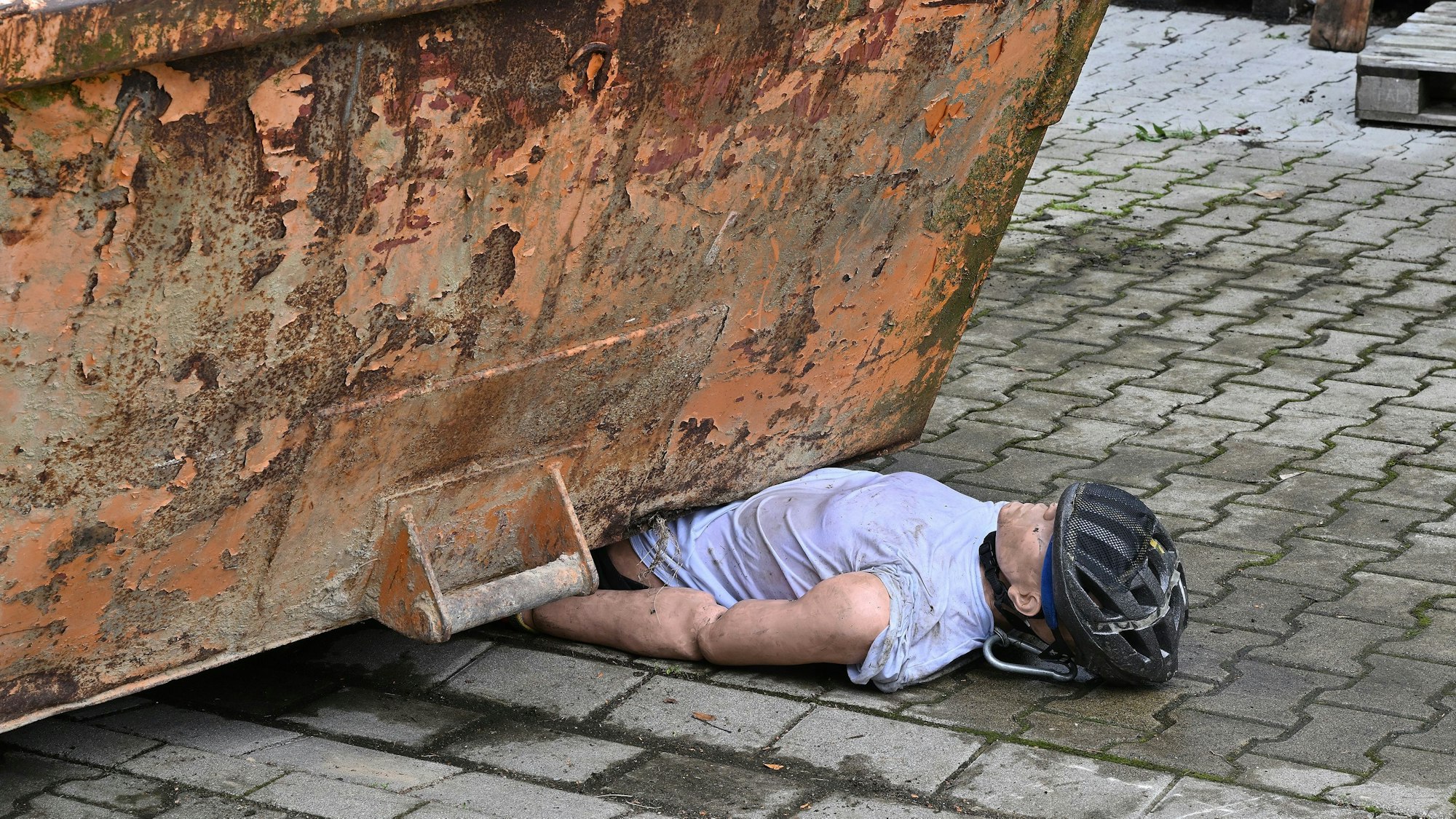 Eine Puppe ist unter einem Container eingeklemmt.