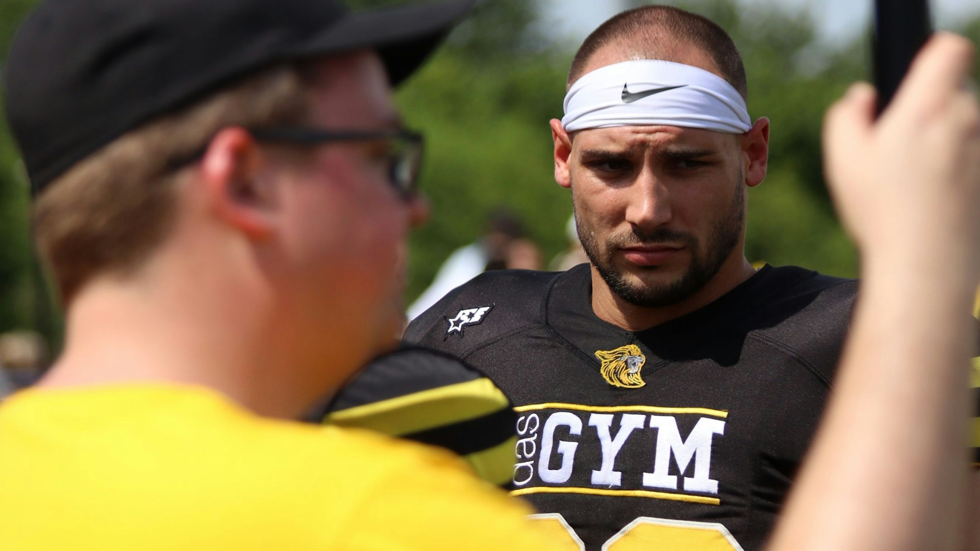David Aigner mit weißem Stirnband, im Vordergrund unscharf der Kameramann.
