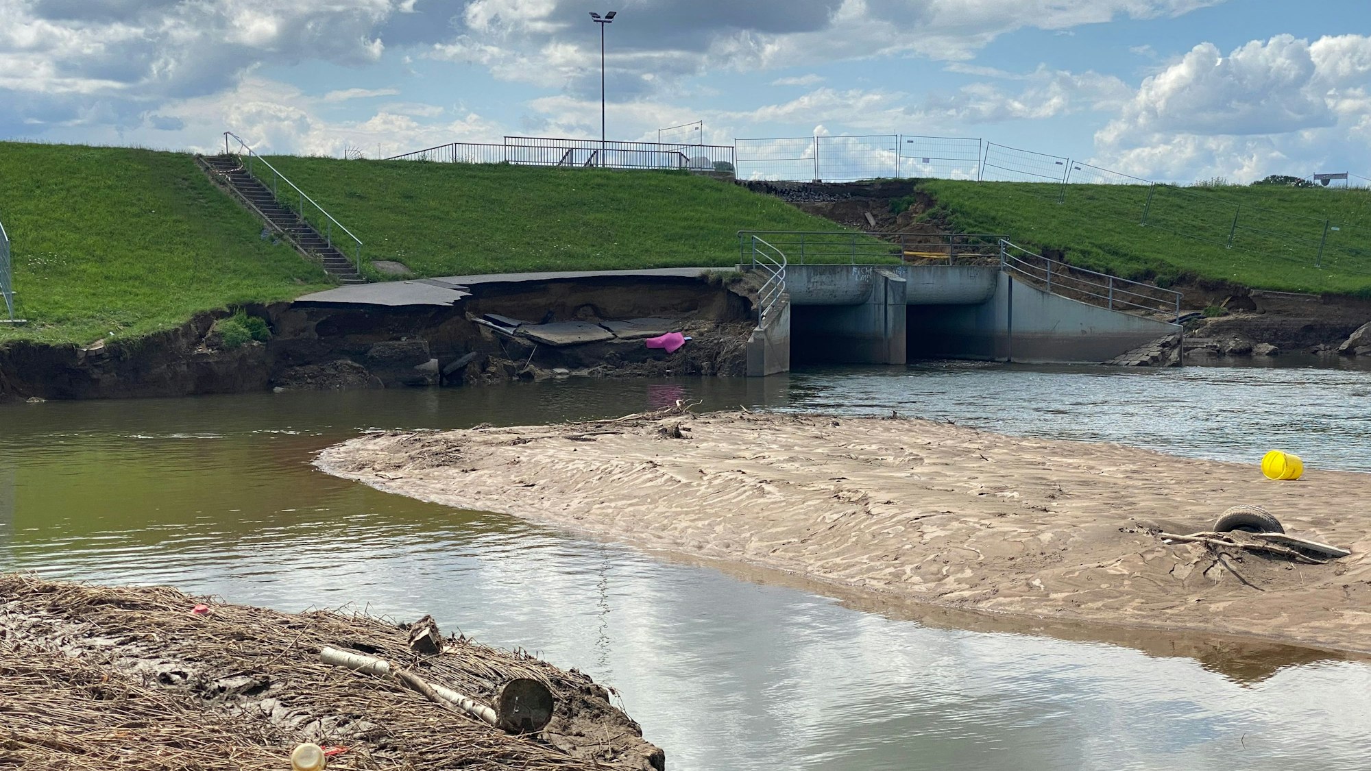Der Damm des Hochwasserbeckens ist beschädigt, davor steht das Gelände unter Wasser.
