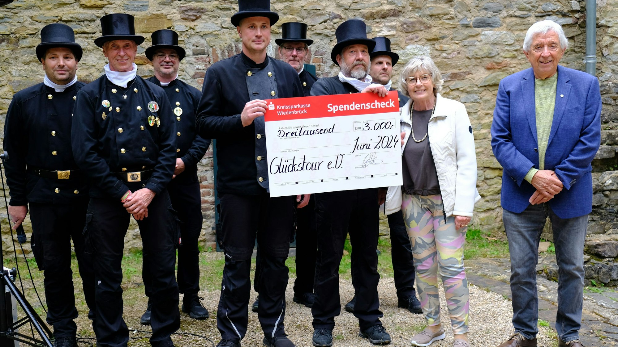 Eine Gruppe von Schornsteinfegern überreicht einen Spendenscheck an Kathi und Willi Greuel von der Hilfsgruppe Eifel.