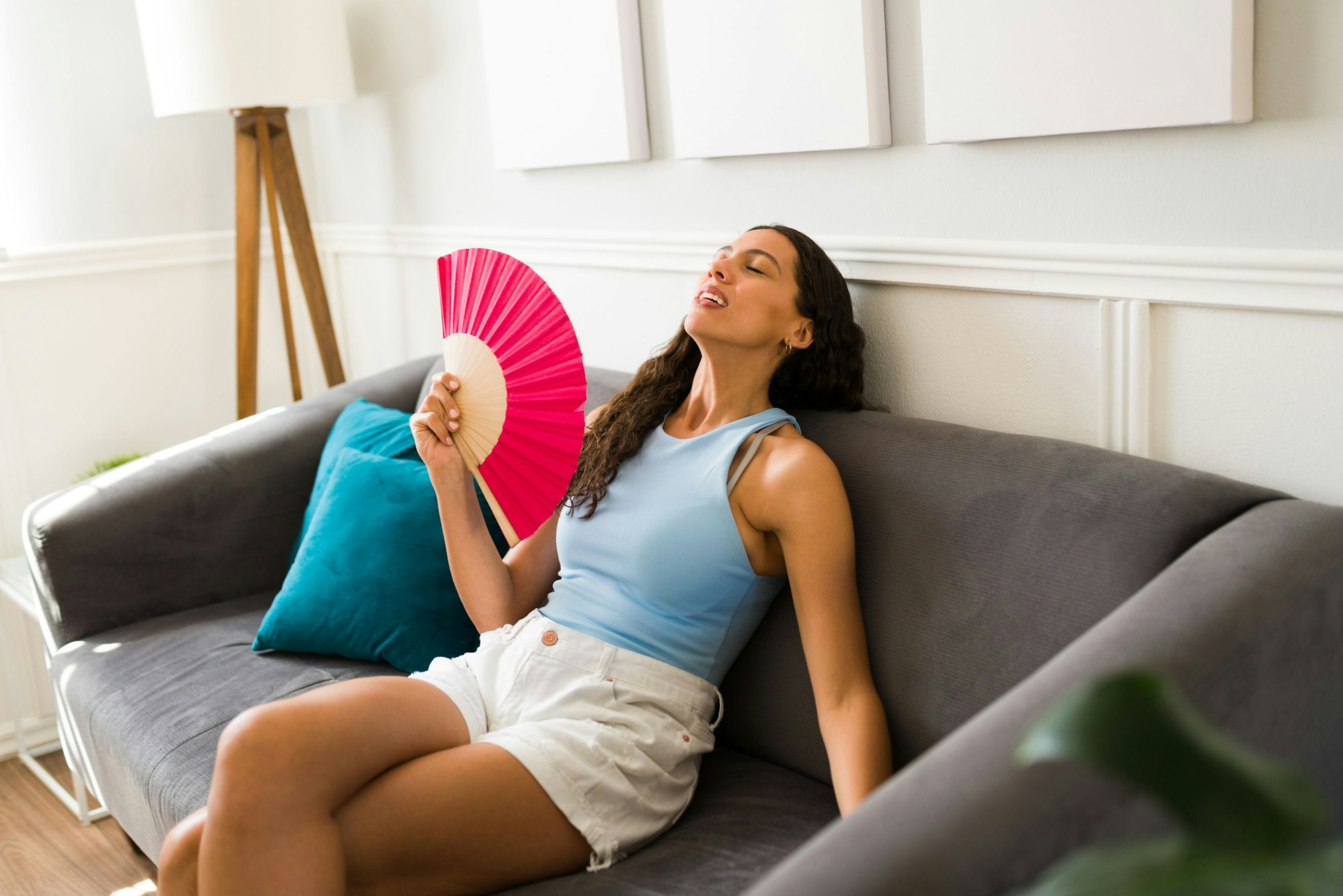Frau sitzt bei großer Hitze auf der Couch und wedelt sich frische Luft mit dem Fächer zu.