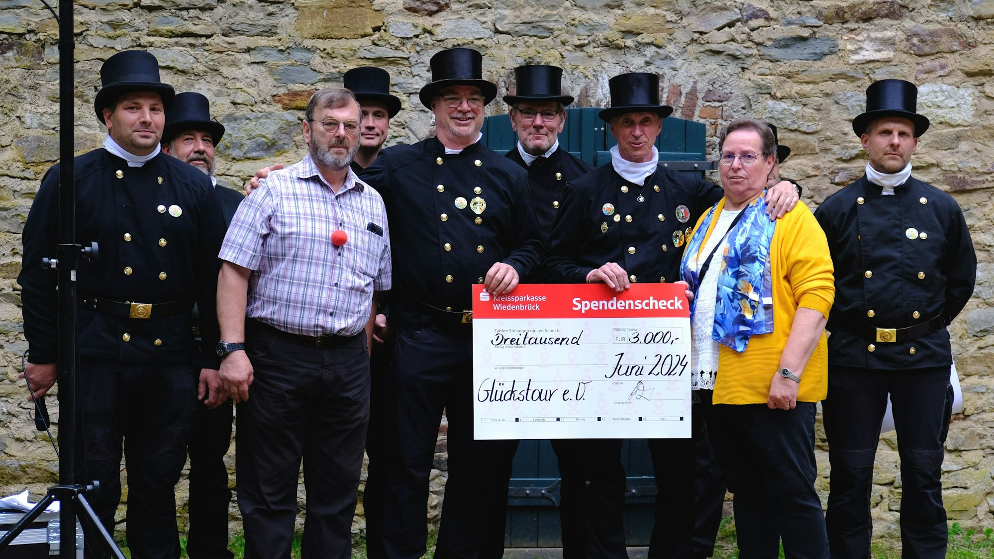 Mehrere Schornsteinfeger mit traditioneller Berufskleidung inklusive Zylinder überreichen einen symbolischen Spendenscheck.