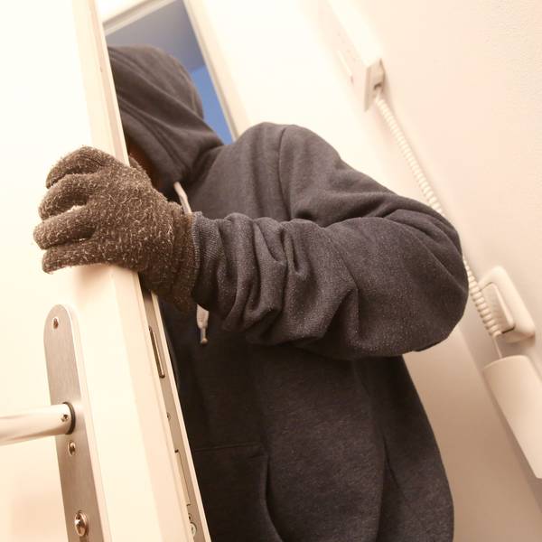 Das Bild ist ein Symbolfoto und zeigt, wie eine maskierte Person in eine Wohnung eindringt.