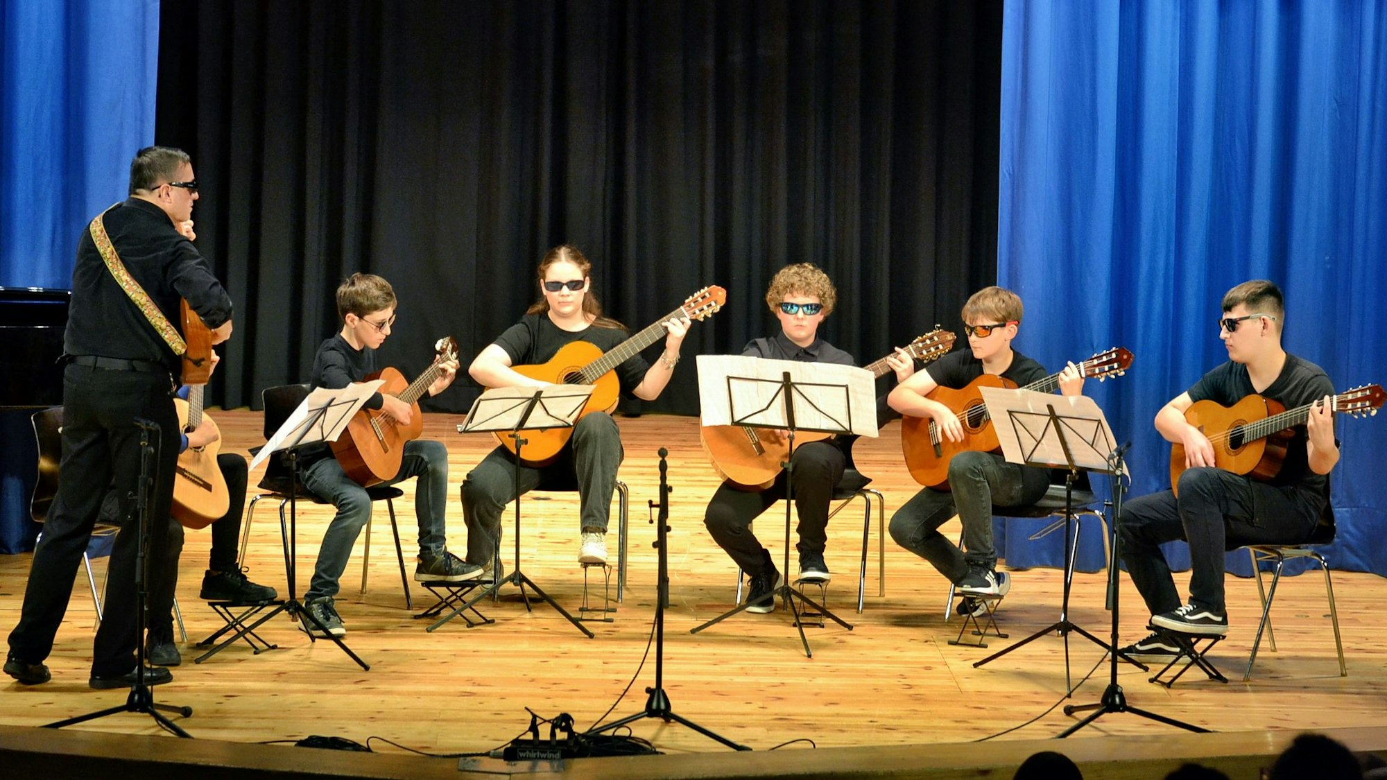 Die Mitglieder des Gitarrenensembles sitzen nebeneinander auf Stühlen, vor ihnen Notenständer.