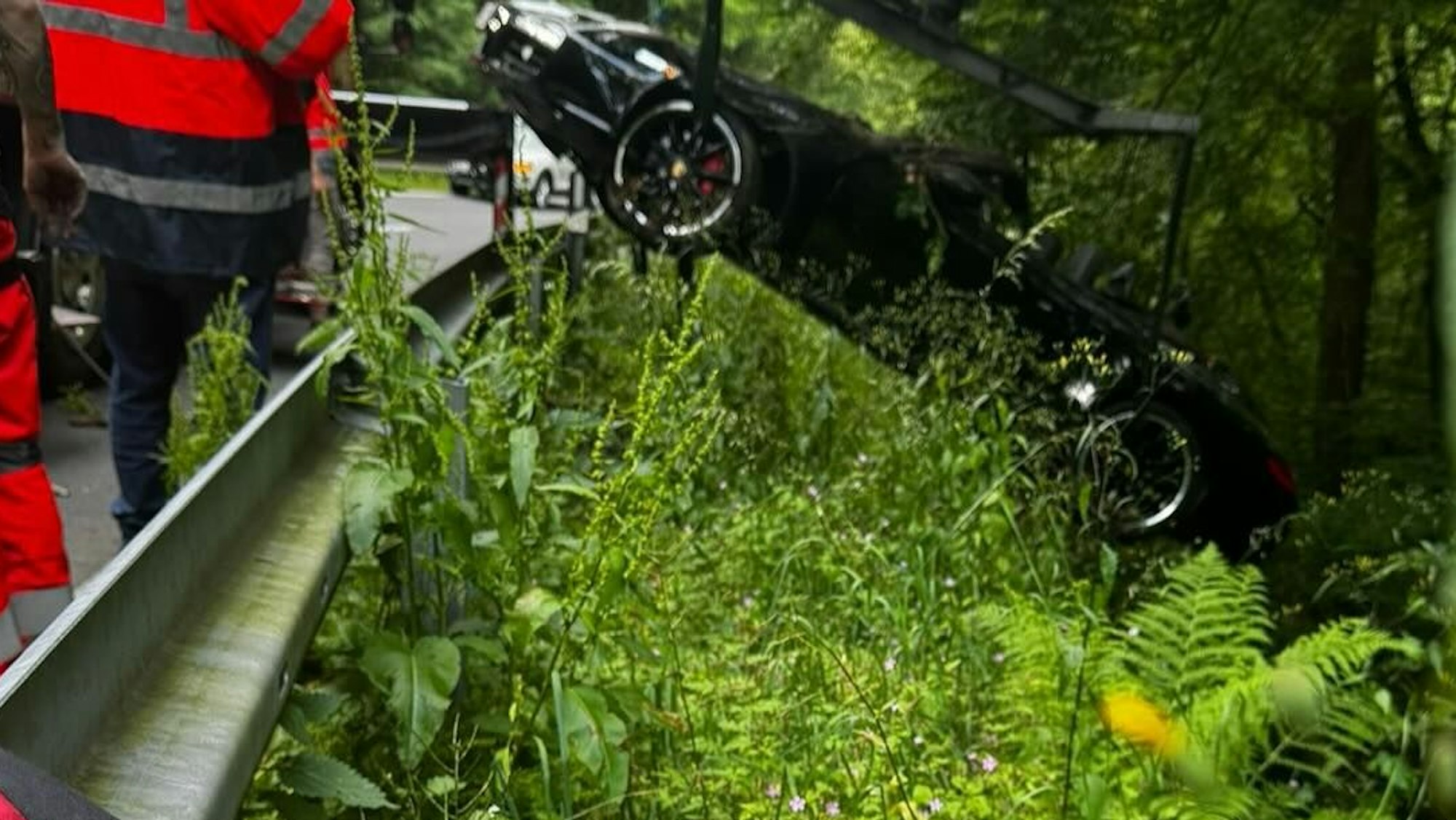 Ein Kran eines Abschleppwagens hebt einen Porsche über eine Leitplanke.