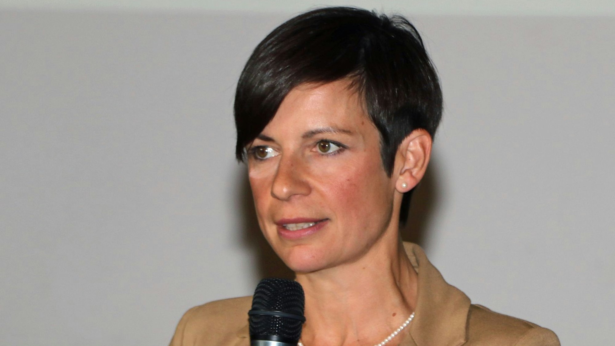 Zu sehen ist eine Frau mit dunklen Haaren vor einem hellen Hintergrund.