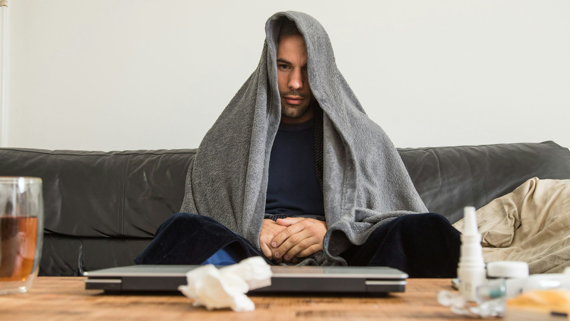 Ein Mann sitzt erkältet auf einem Sofa. (Symbolbild)