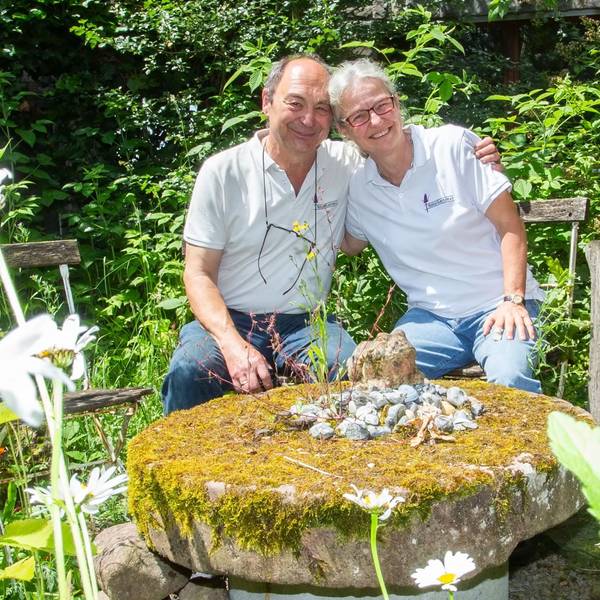 Ein Paar sitzt auf Gartenstühlen im Grünen und umarmt sich.