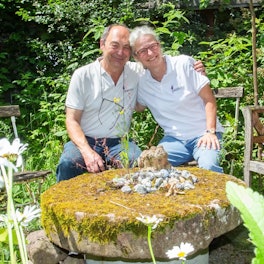 Ein Paar sitzt auf Gartenstühlen im Grünen und umarmt sich.