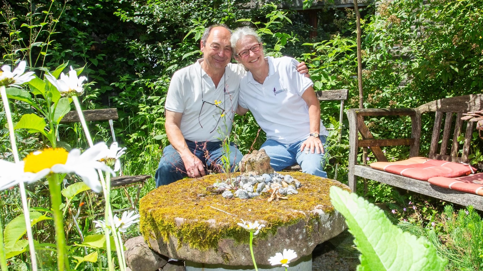 Ein Paar sitzt auf Gartenstühlen im Grünen und umarmt sich.