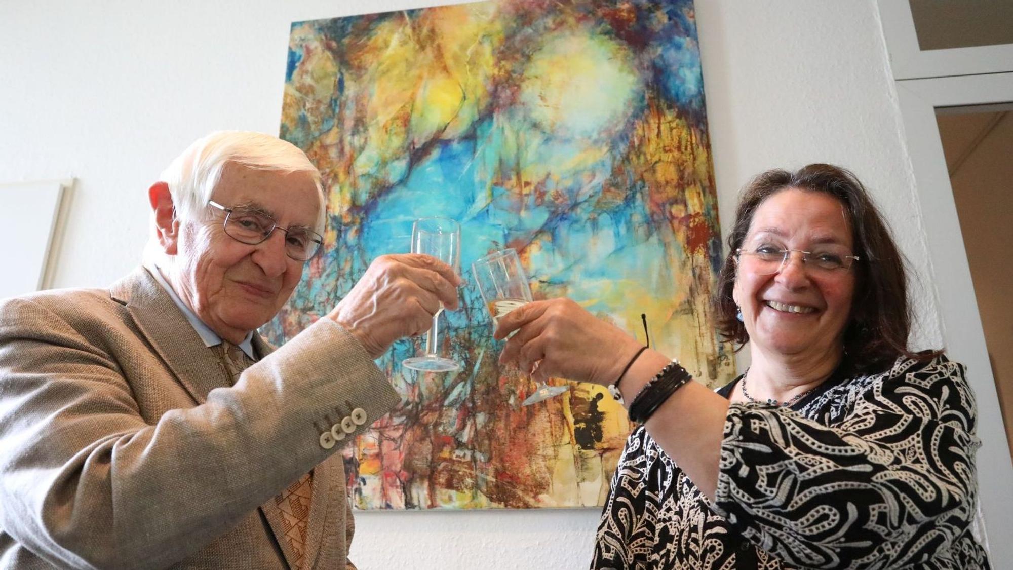 Ein Mann und eine Frau stoßen vor einem Kunstwerk mit einem Glas Sekt an.