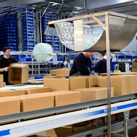 Das Foto zeigt eine Halle der Firma Rüggeberg mit vielen Paketen und einigen Mitarbeitern