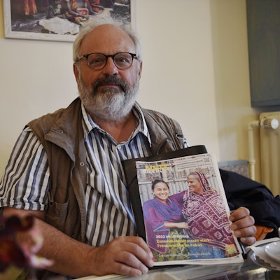Joachim Berg sitzt im Fair Café in Zülpich und hält einen Flyer der Hilfsorganisation Netz Bangladesch in die Kamera.