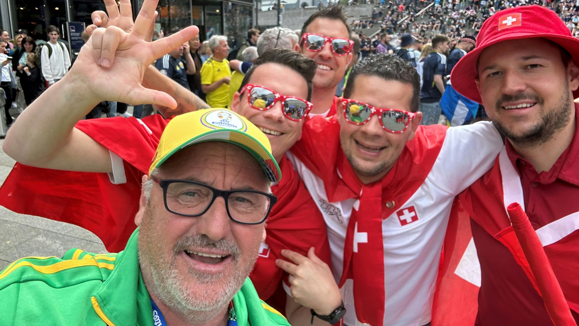 EM-Volunteer Mike Pütz in Köln mit vier jubelnden Fußballfans aus der Schweiz in rot-weißem Outfit.