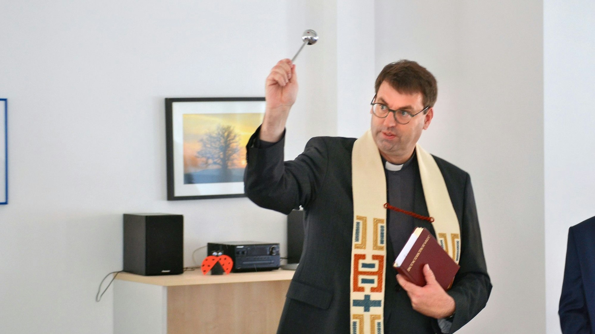 Kreisdechant Guido Zimmermann trägt einen schwarzen Anzug und helle Stola. Er hält ein Aspergill in der Hand und segnet ein Zimmer der Caritas-Tagespflege in Euskirchen ein.