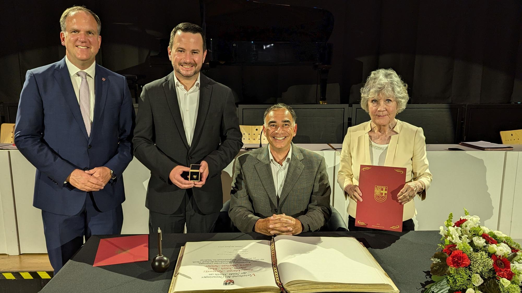Der Bürgermeister und die ausgezeichneten Ratsmitglieder mit Urkunde, Schmuckschatulle und dem aufgeklappten Goldenen Buch auf einem Tisch.