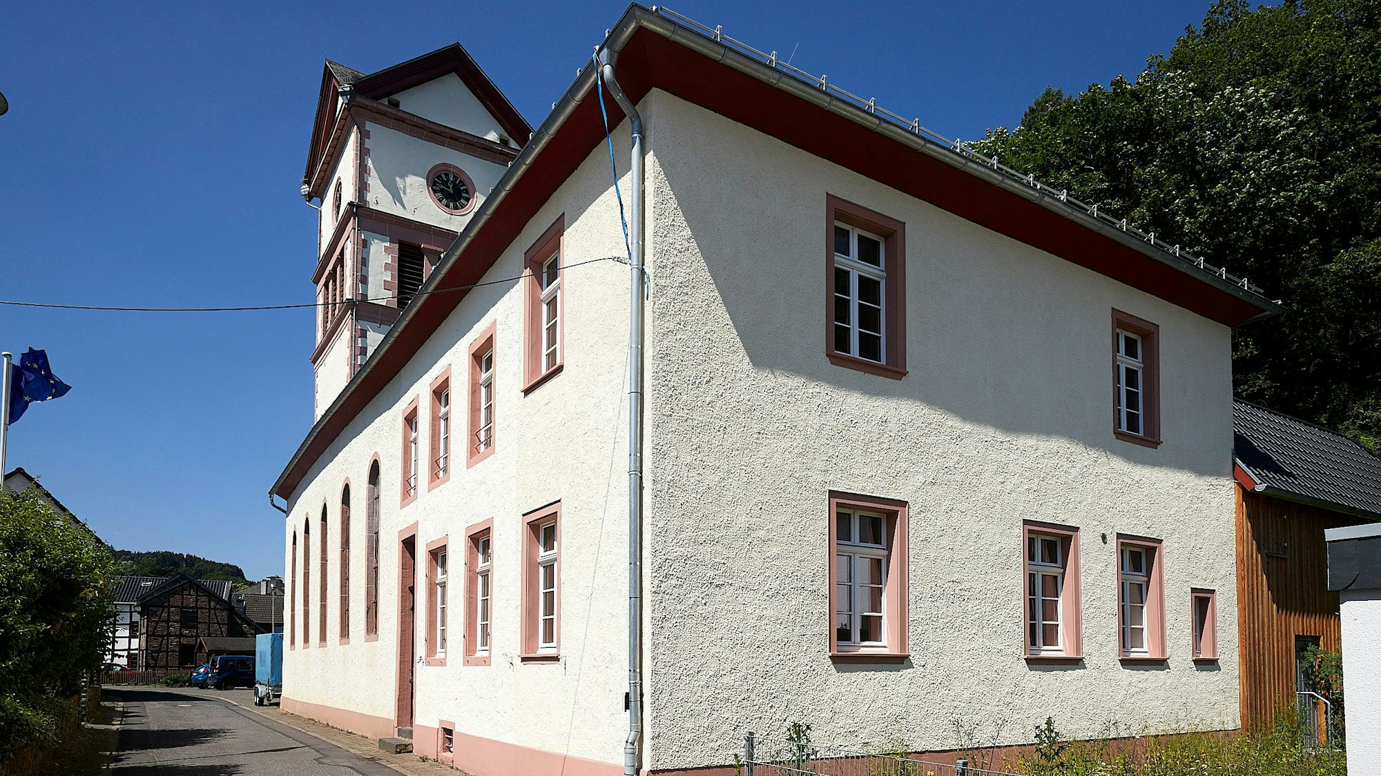 Im Vordergrund ist das Alte Pfarrhaus an der evangelischen Kirche in Hellenthal zu sehen, dahinter lugt der Kirchturm hervor.