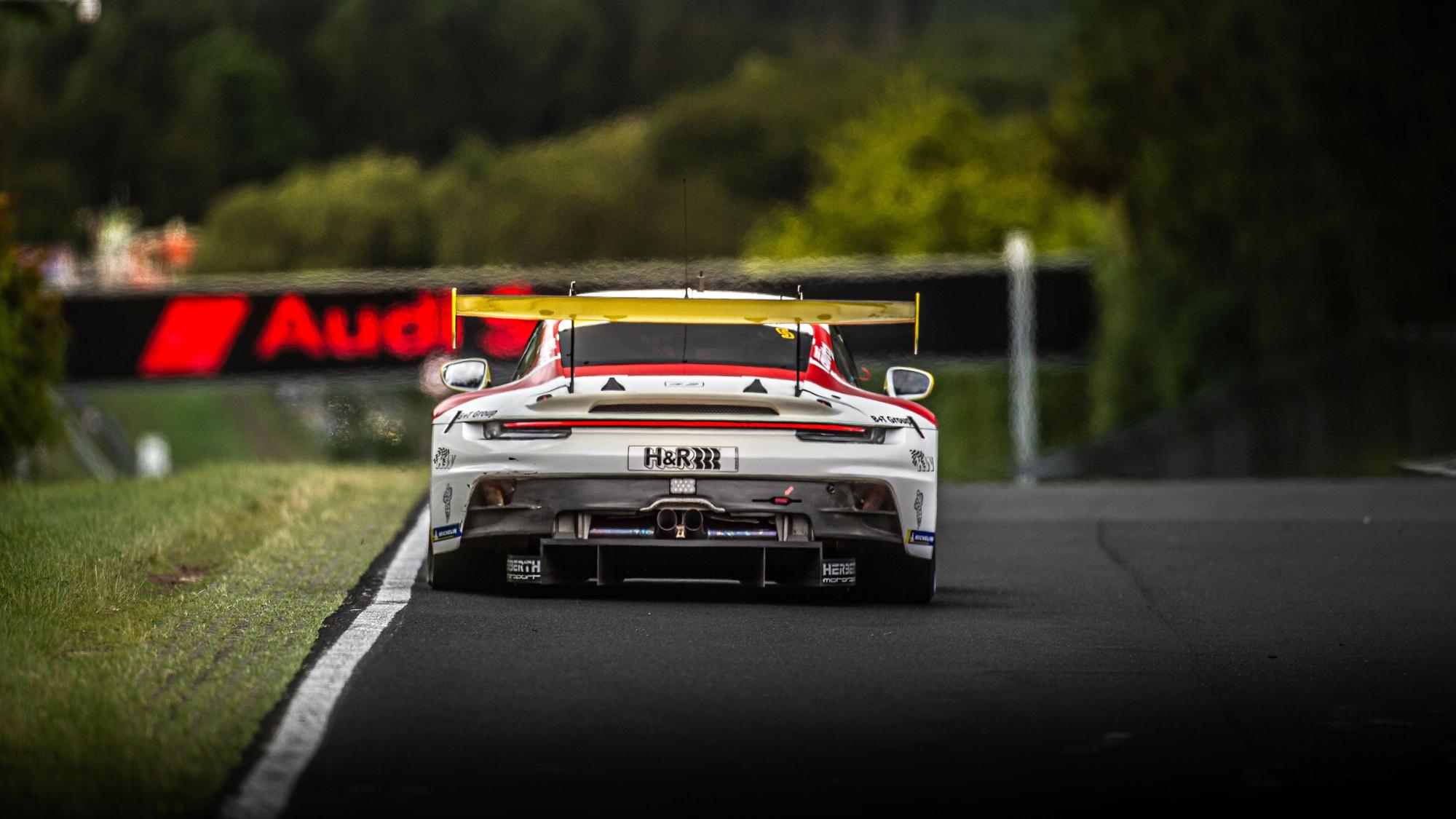 Frank Stippler fährt im Porsche, der von hinten zu sehen ist, auf eine Audi-Reklame zu.