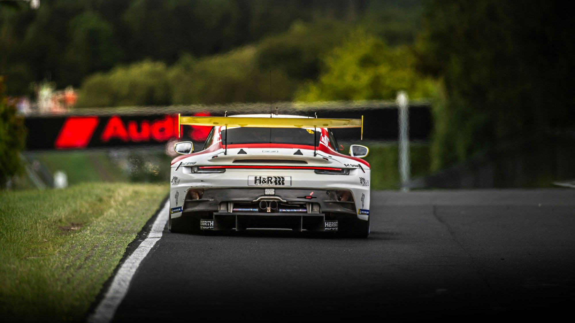 Frank Stippler fährt im Porsche, der von hinten zu sehen ist, auf eine Audi-Reklame zu.