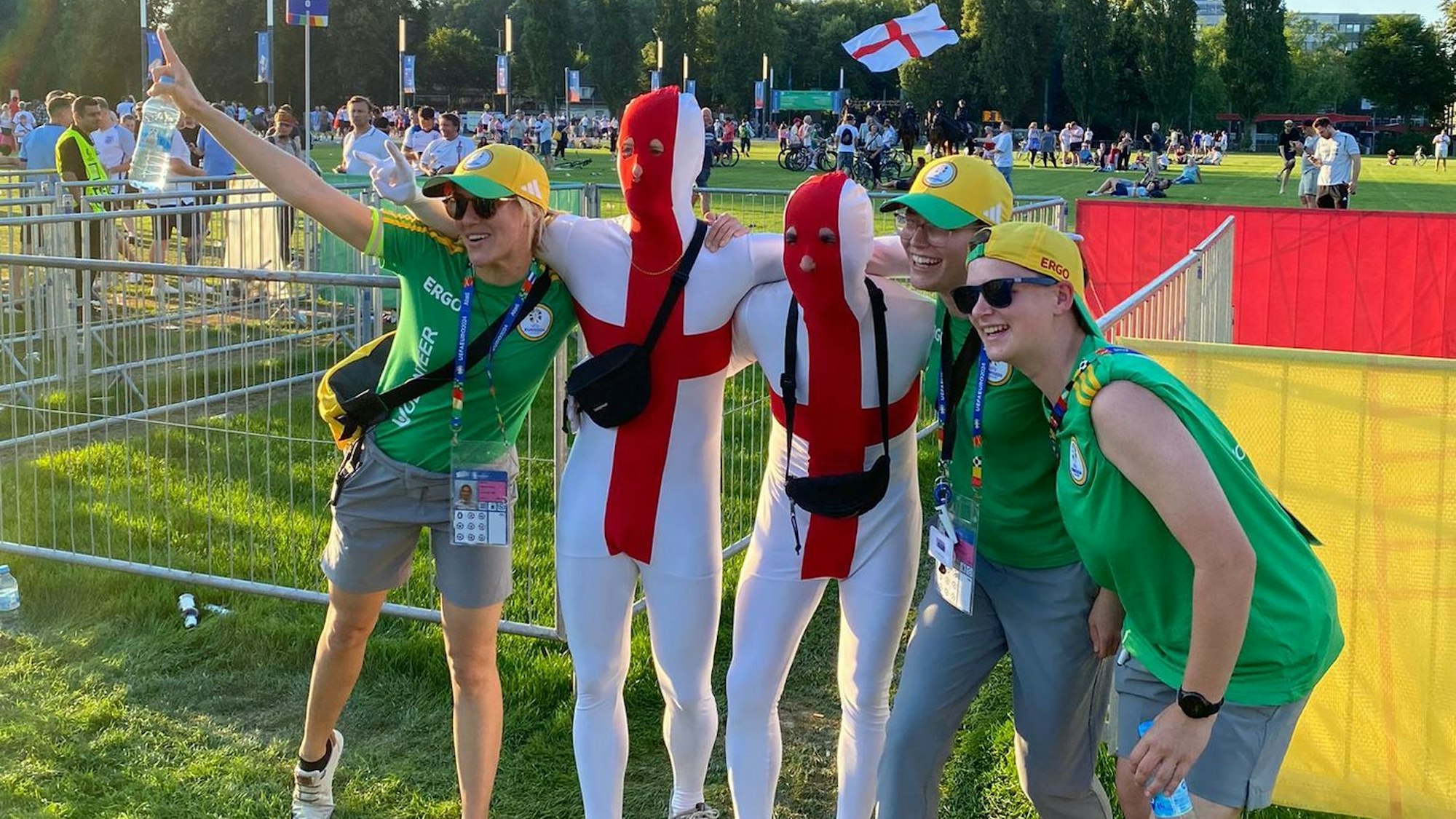 Laurie Simon und zwei weitere EM-Volunteers posieren mit Fans, die rot-weiße Ganzkörperanzüge tragen.