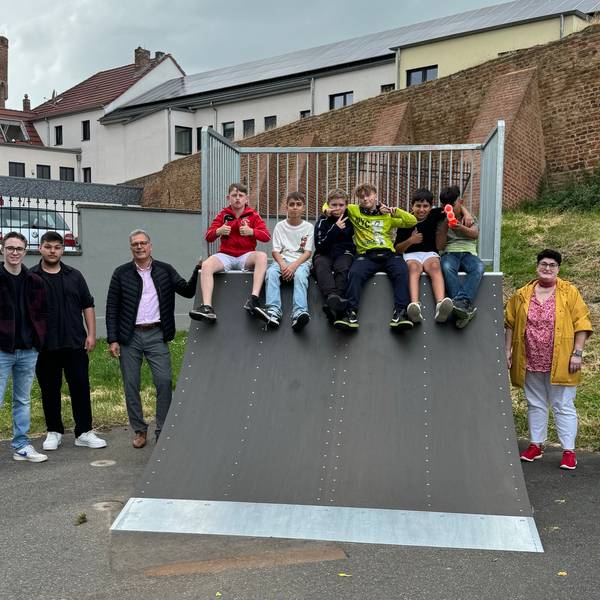 Die Beteiligten stehen neben einer Skaterampe am Frankengraben, auf der sechs Jugendliche sitzen.
