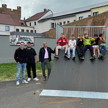 Die Beteiligten stehen neben einer Skaterampe am Frankengraben, auf der sechs Jugendliche sitzen.