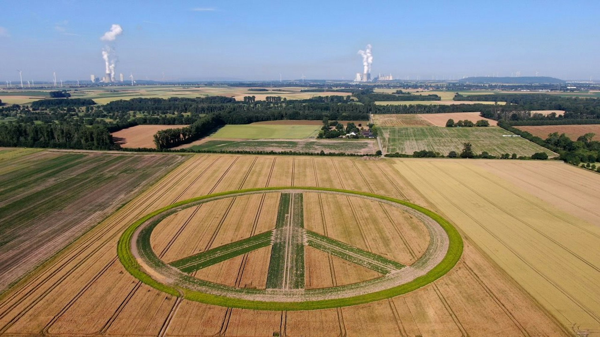 Im Vordergrund ist das Peace-Zeichen zu sehen, im Hintergrund zwei Kraftwerke.