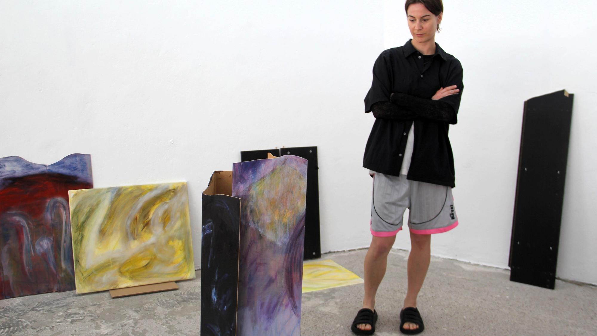 Kunstschaffende Person neben Kunstwerken