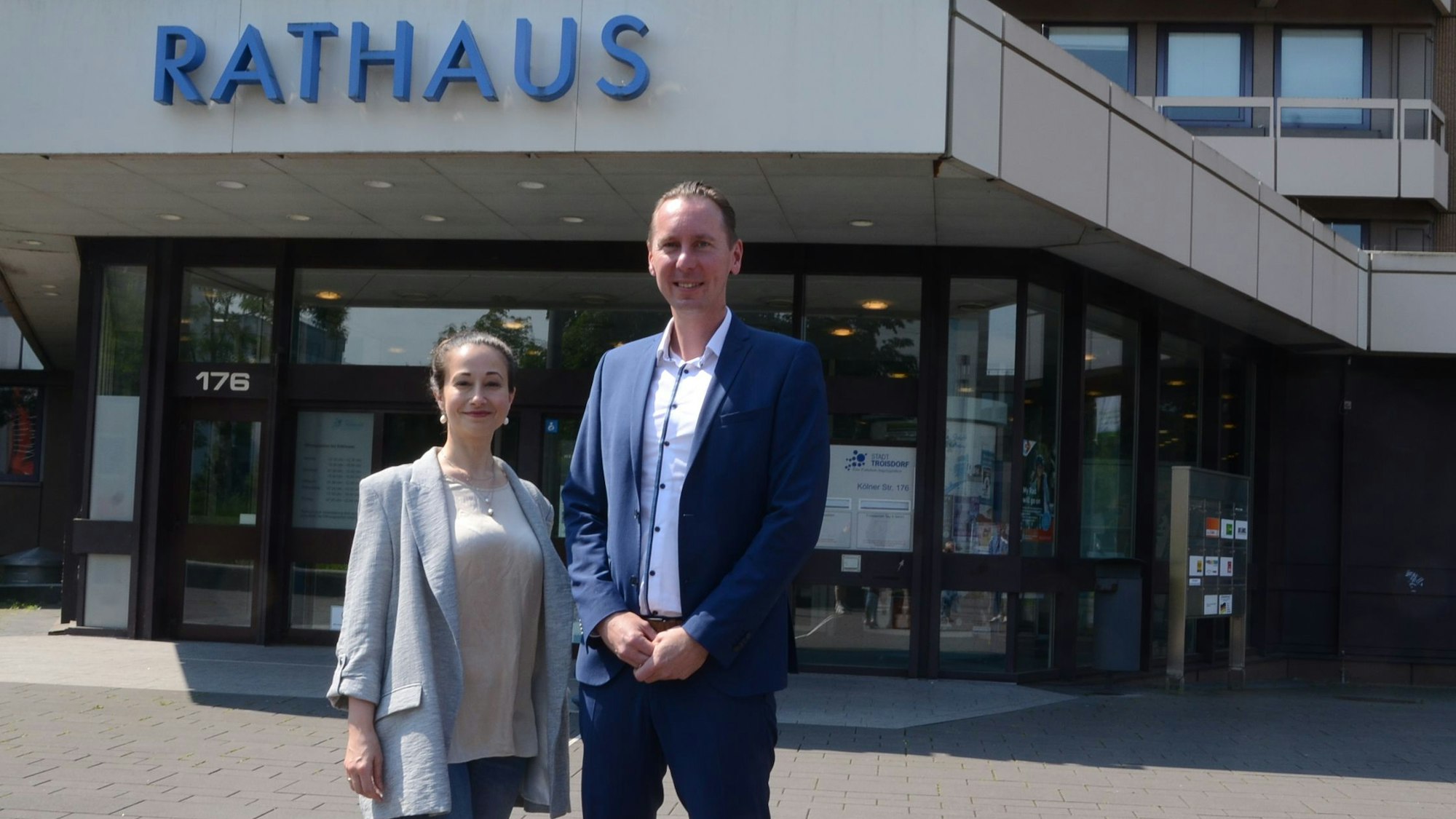 Ein Mann und eine Frau vor einem Verwaltungsgebäude. Über dem Eingang steht "Rathaus"
