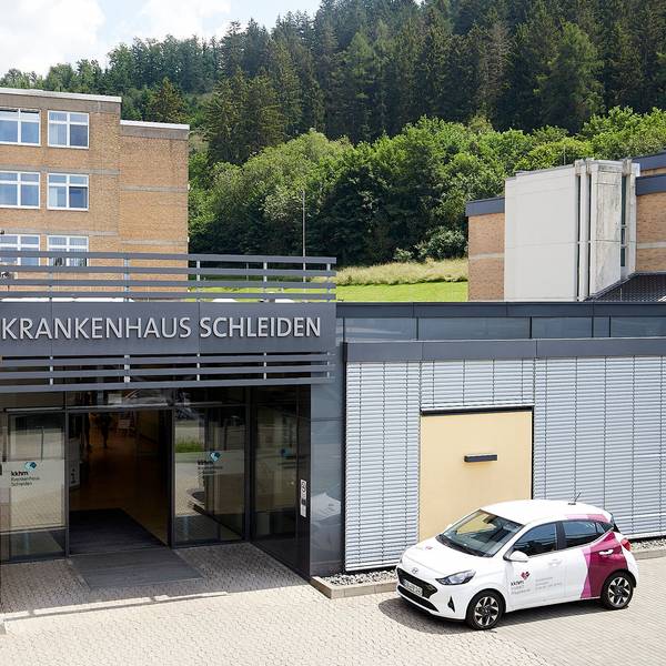 Das Bild zeigt den Haupteingang des Krankenhauses Schleiden, davor parkt ein Auto.