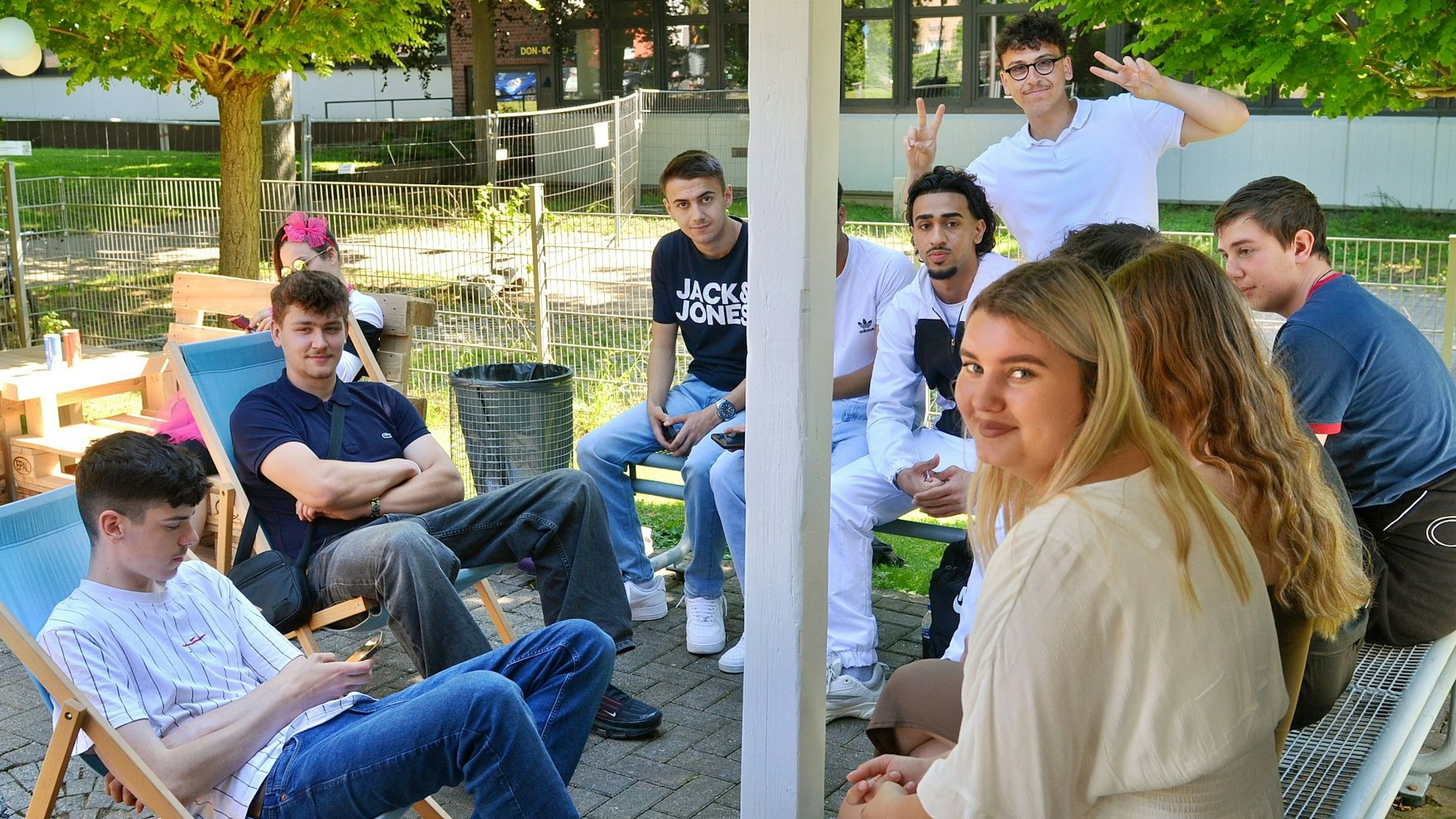 Schülerinnen und Schüler des Thomas-Eßer-Berufskollegs sitzen im Freien zusammen und blicken in die Kamera.