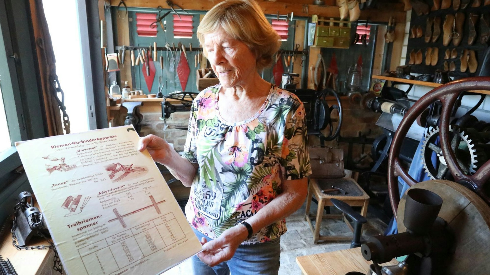 Eine Frau hält in einer alten Schusterei in Schild in den Händen.