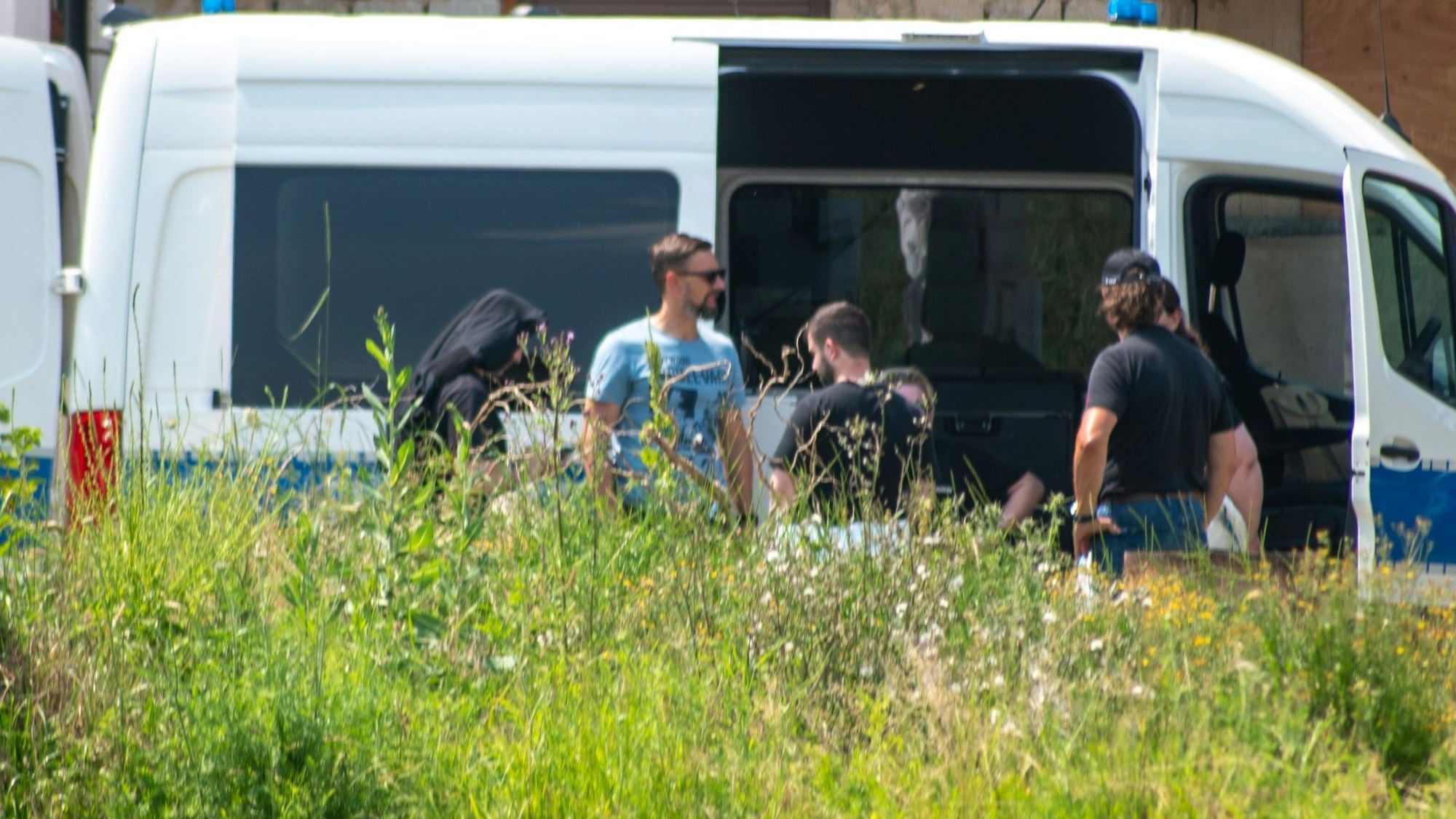 Mitarbeiter des LKA sind in Füssenich im Einsatz. Sie stehen vor einem blau-weißen Polizei-Auto.