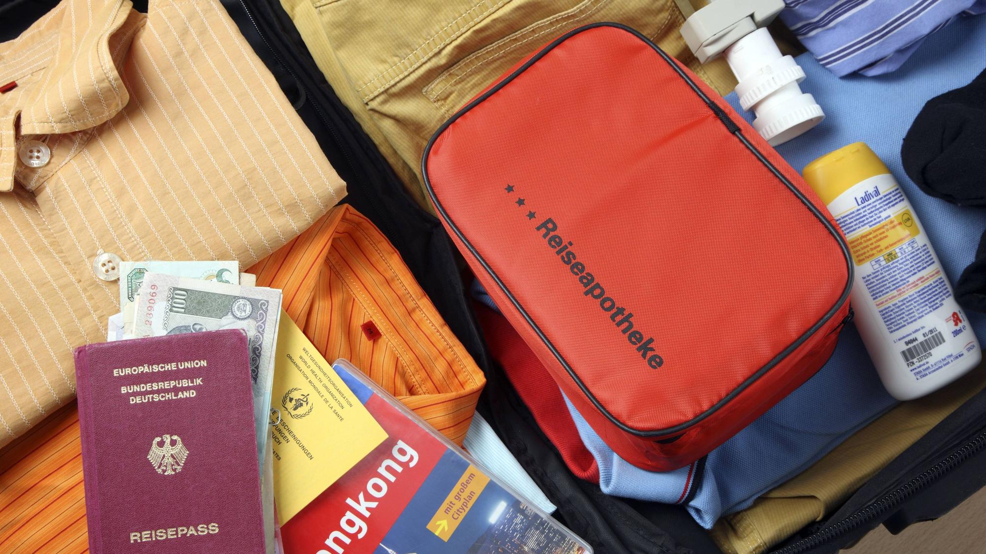 Auf einem gepackten, geöffneten Koffer liegt ein Medizin-Täschchen mit der Aufschrift Reiseapotheke