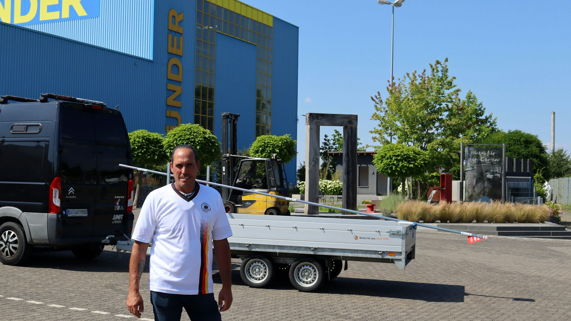 Manfred Gottschalk steht im Deutschland-Trikot auf dem Parkplatz des Baustoffhandels Bünder. Im Hintergrund ein Gabelstapler.