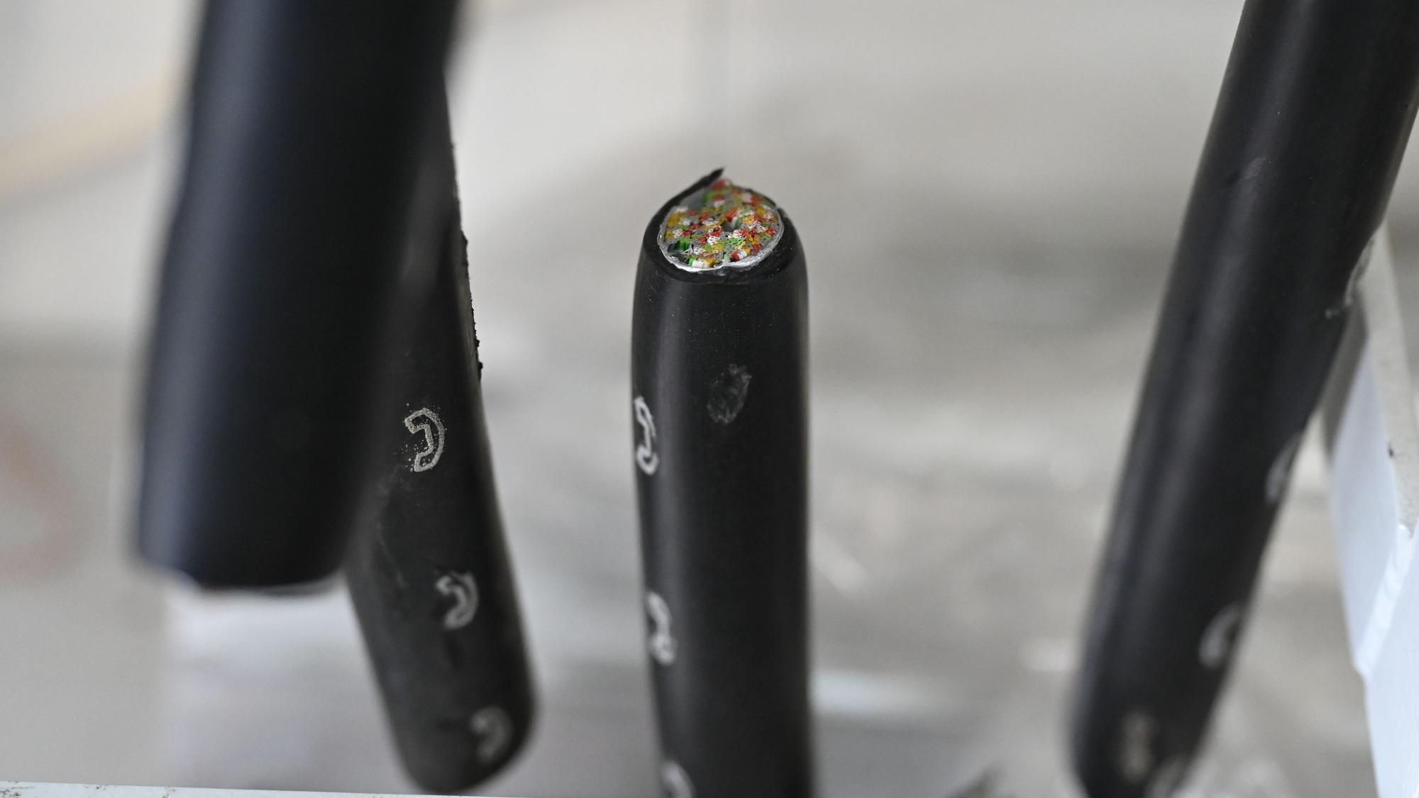 Dicke, schwarze Kabel mit weißen Telefonsymbolen sind durchgeschnitten. In einem sieht man die zahlreichen Kupferadern.