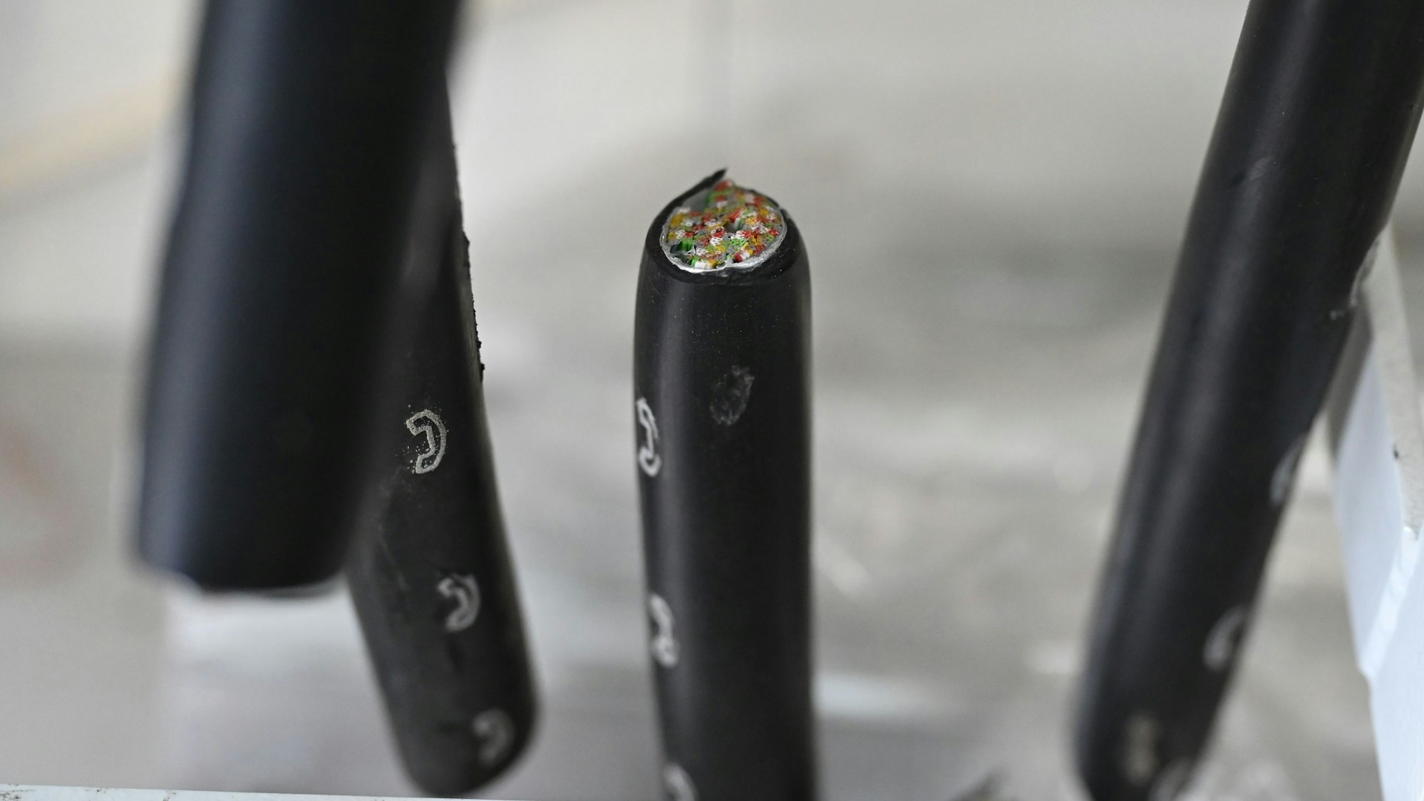 Dicke, schwarze Kabel mit weißen Telefonsymbolen sind durchgeschnitten. In einem sieht man die zahlreichen Kupferadern.