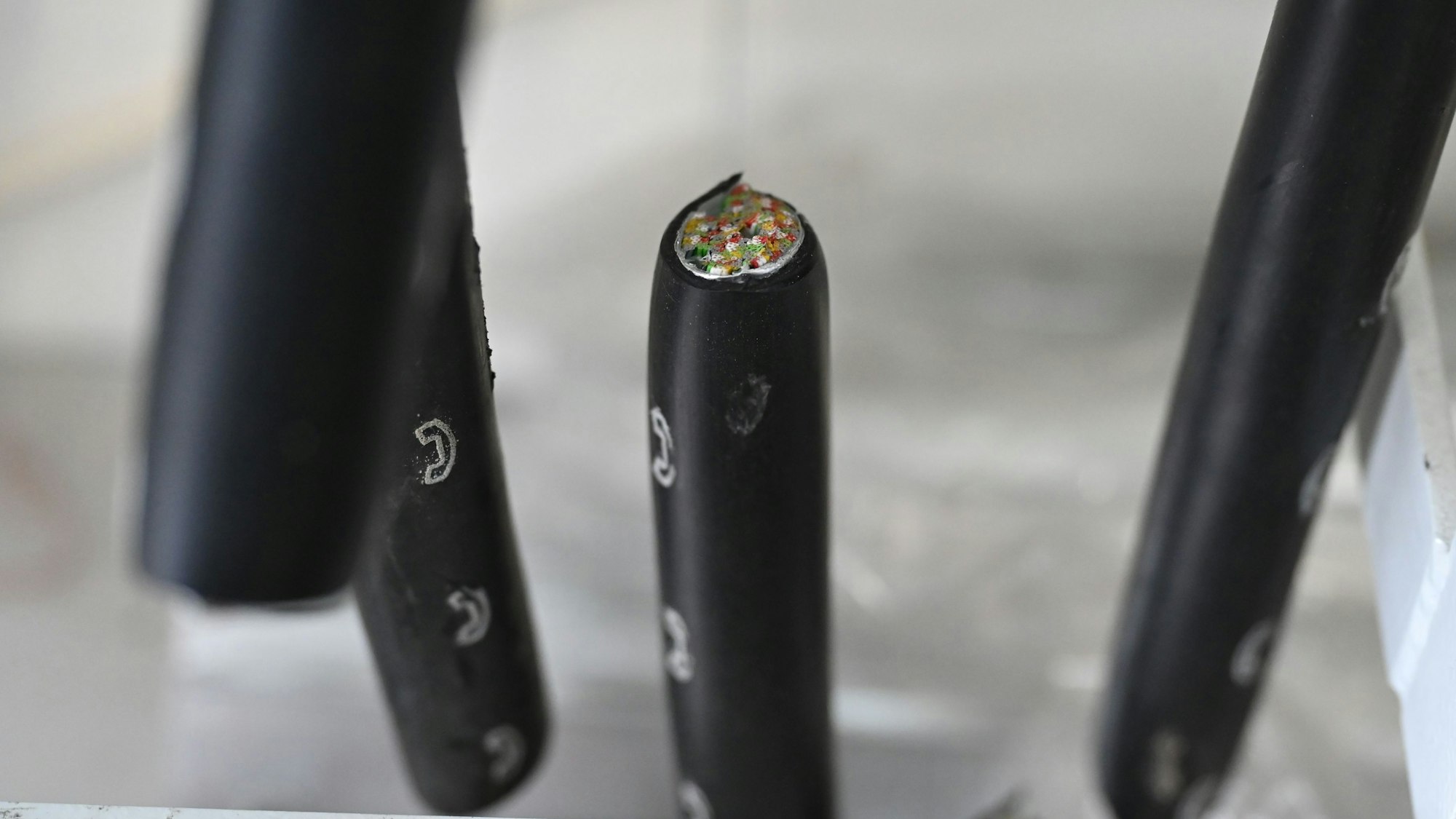 Dicke, schwarze Kabel mit weißen Telefonsymbolen sind durchgeschnitten. In einem sieht man die zahlreichen Kupferadern.