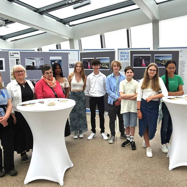 Die Schüler und Lehrer stehen vor Stellwänden mit den Zeichnungen über Holocaust-Opfer.