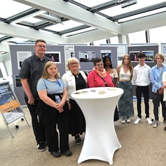 Die Schüler und Lehrer stehen vor Stellwänden mit den Zeichnungen über Holocaust-Opfer.