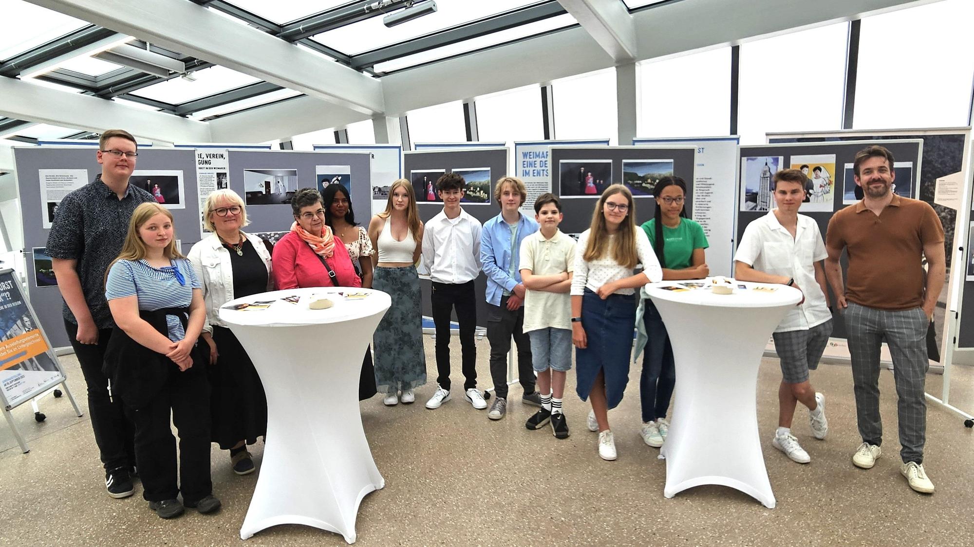 Die Schüler und Lehrer stehen vor Stellwänden mit den Zeichnungen über Holocaust-Opfer.