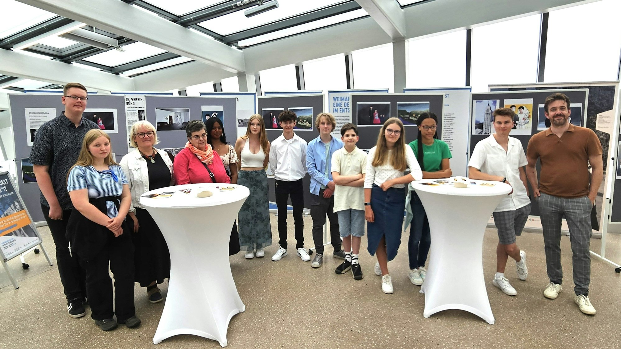 Die Schüler und Lehrer stehen vor Stellwänden mit den Zeichnungen über Holocaust-Opfer.