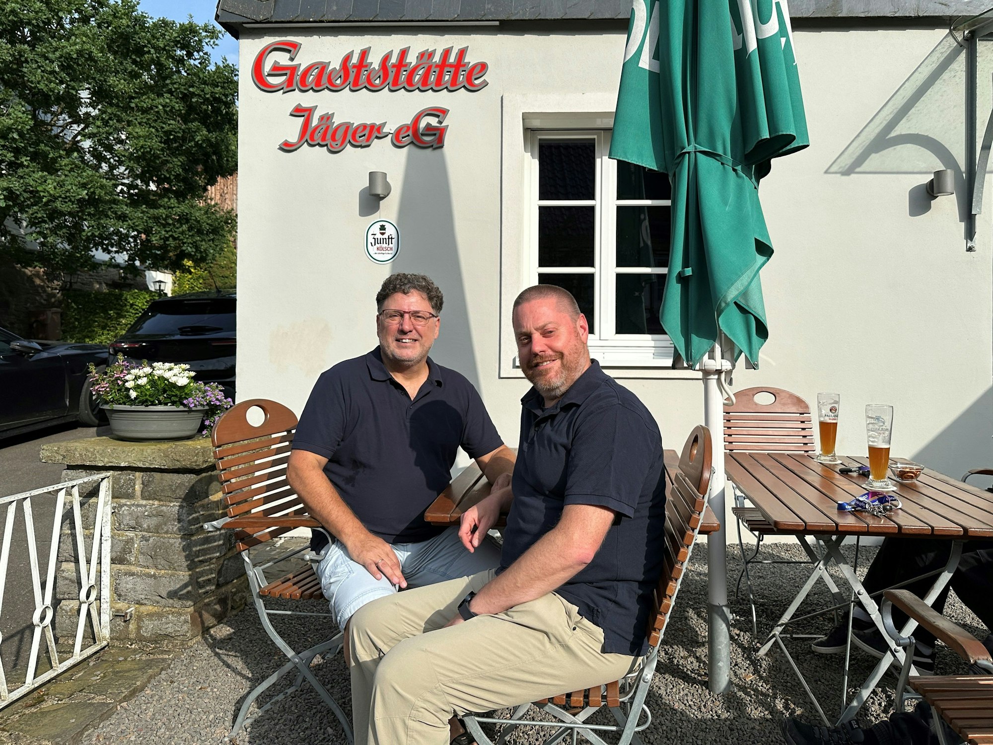 Andreas Döhl und Sven Kiebler sitzen vor der Kneipe und blicken in die Kamera.