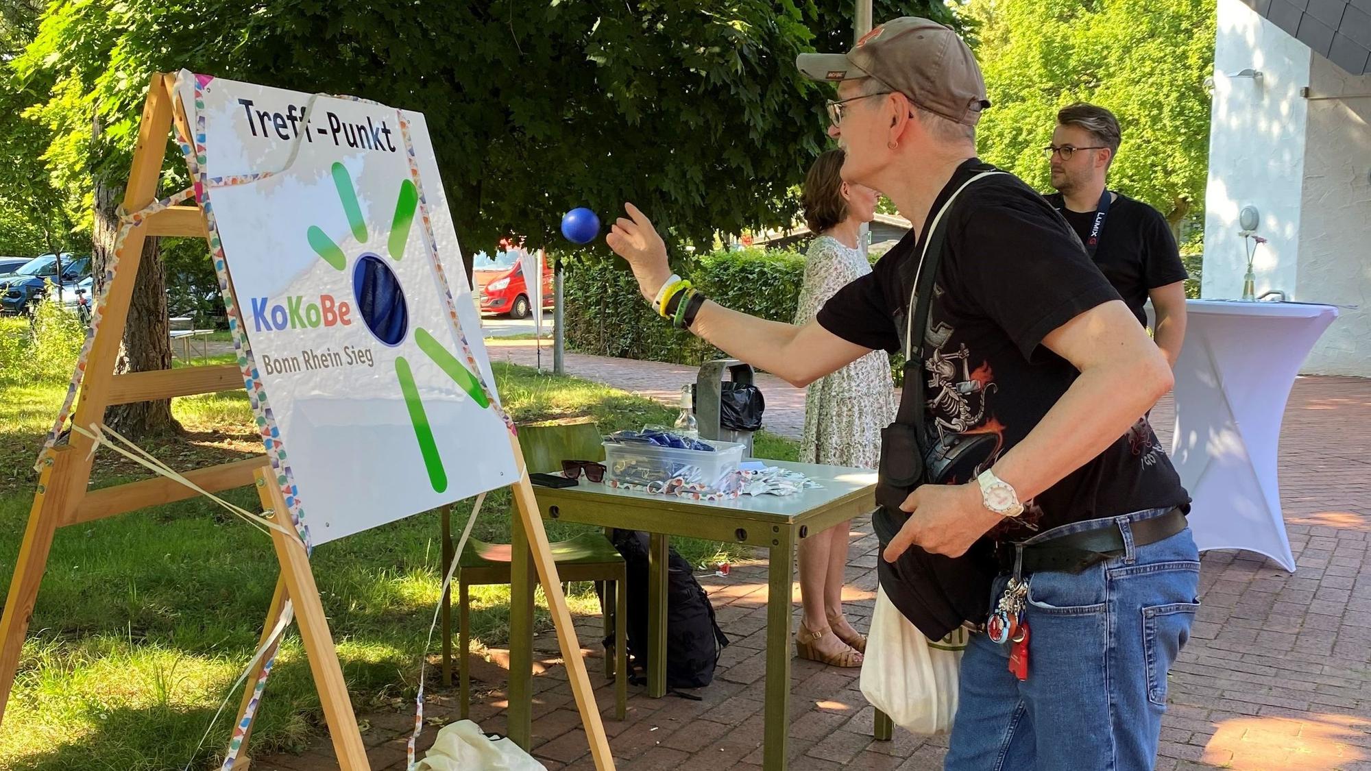 Ein Mann wirft Bälle auf eine bunt gestaltete Tafel mit der Aufschrift "Treff-Punkt"