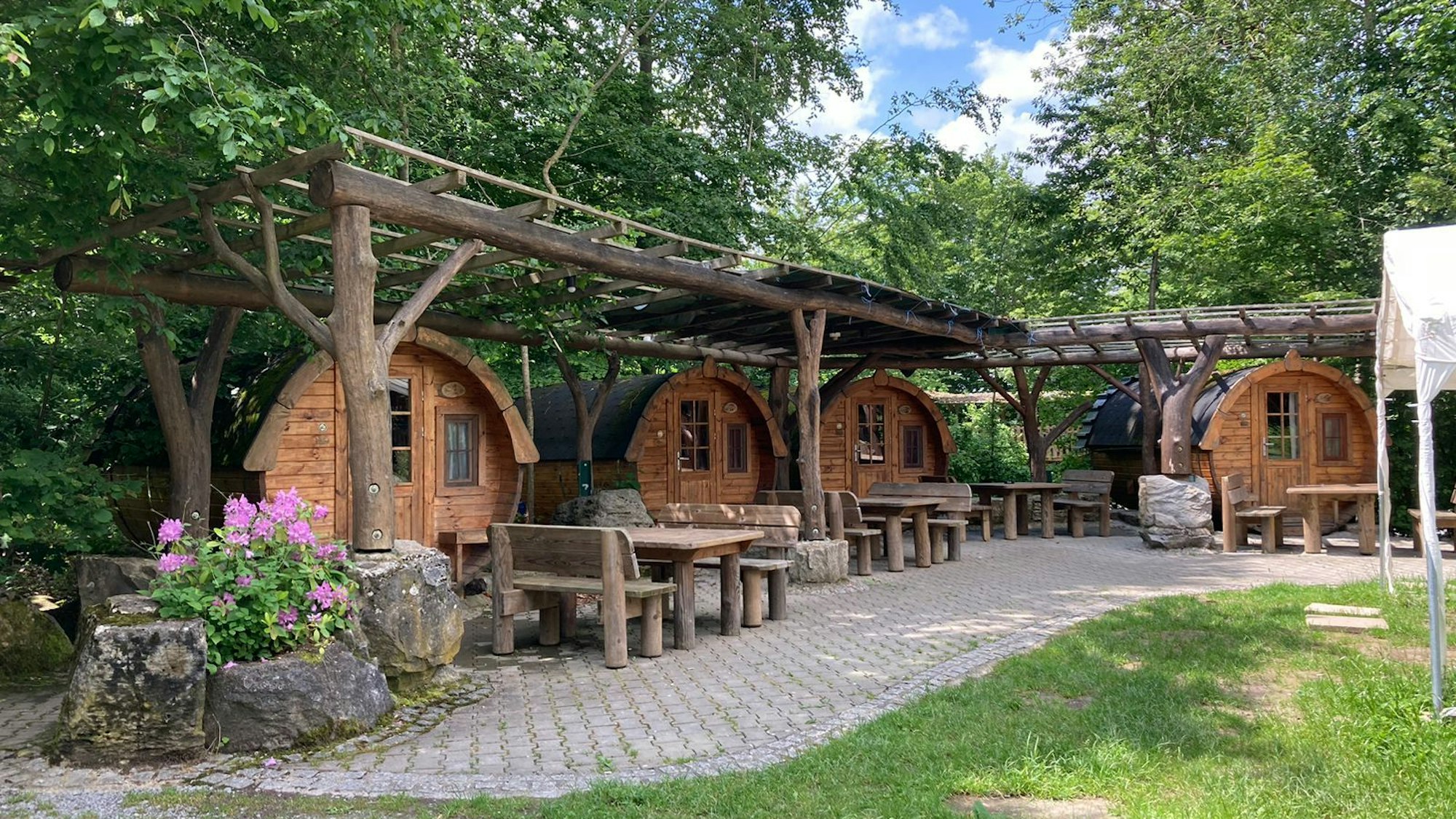 Eine Ansammlung von Holzfässern, die als Unterkunnft dienen, stehen in einem Garten.