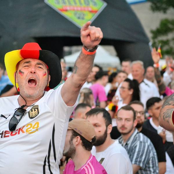 Ein Fan mit Hut in den Deutschlandfarben und mit einem Fan-T-Shirt jubelt und singt beim Public Viewing.