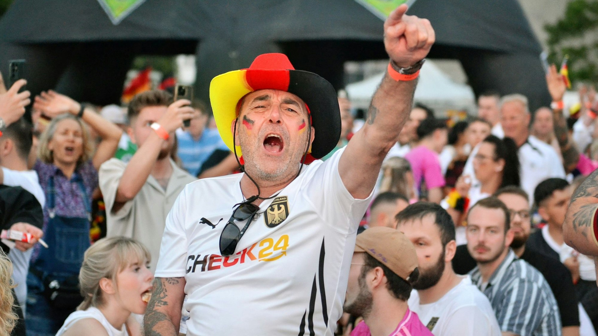 Ein Fan mit Hut in den Deutschlandfarben und mit einem Fan-T-Shirt jubelt und singt beim Public Viewing.