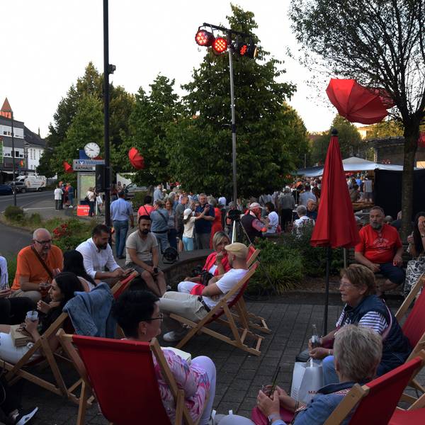 Menschen sitzen beieinander auf roten Liegestühlen.